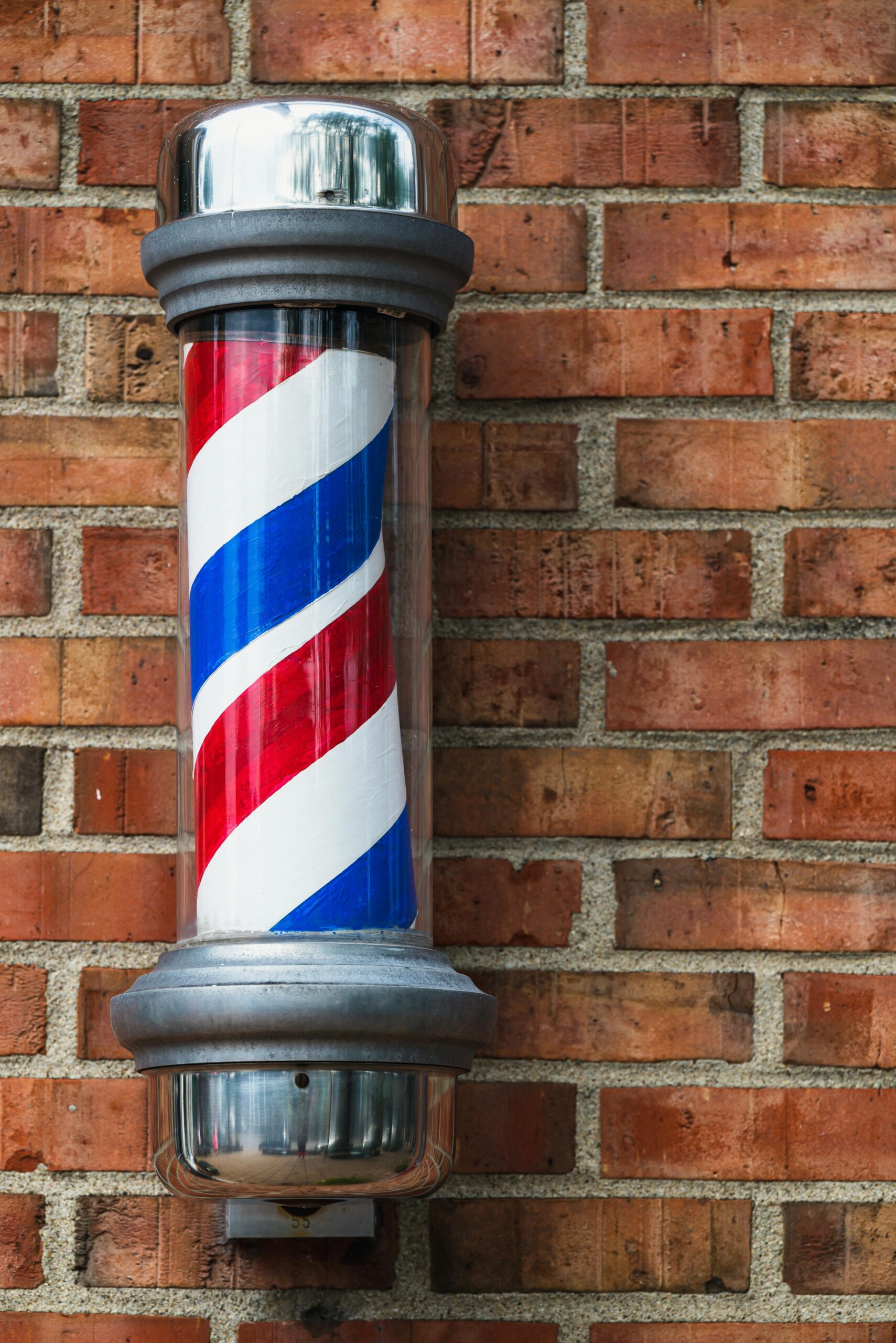 Vertical shot of a traditional barber pole against a red brick wall, symbolizing classic barber culture.